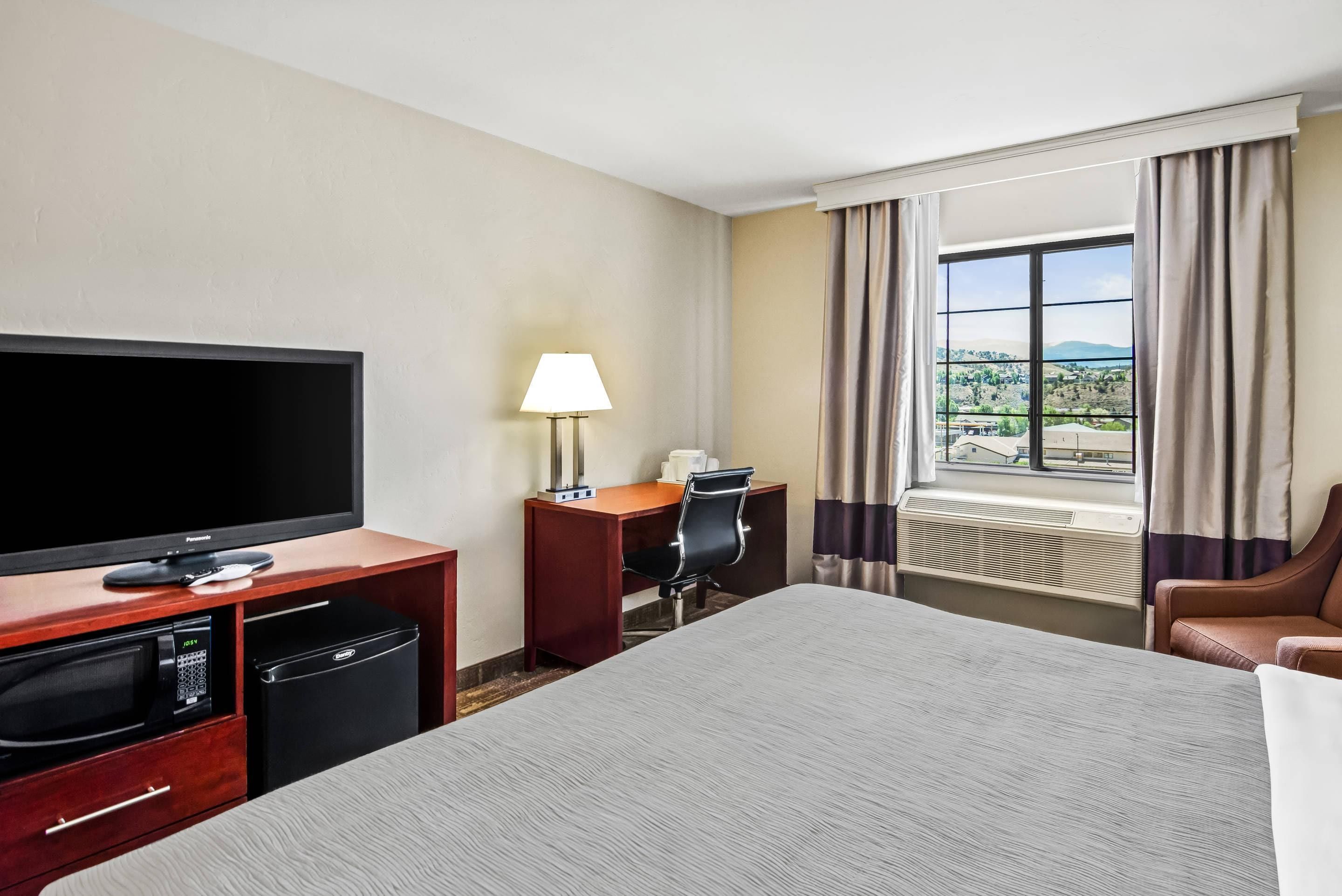 Habitación de hotel con cama, televisión, escritorio, lámpara y vista al exterior.