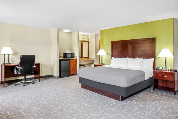 A hotel room with a bed, desk, chair, and a microwave.