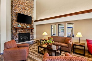 A living room with a brick fireplace, a flat-screen TV, a sofa, two armchairs, a coffee table, and two lamps.
