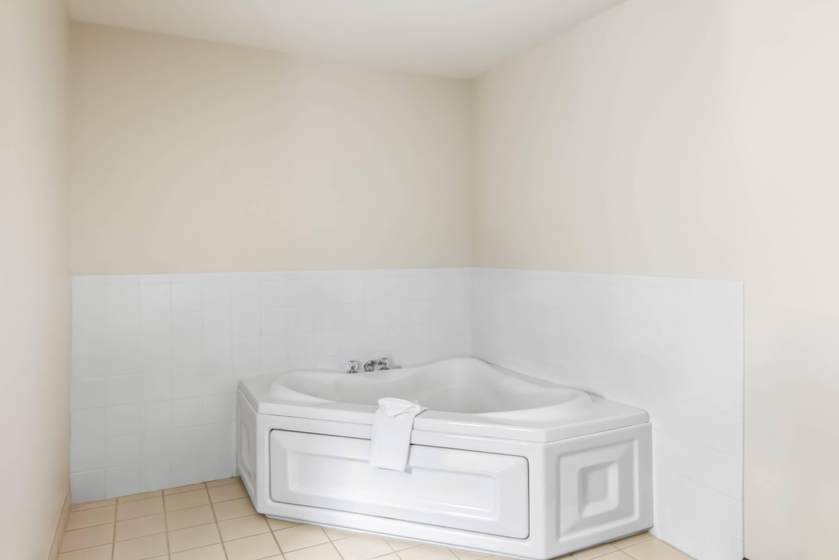 A corner bathroom with a white bathtub, tiled walls, and floor.