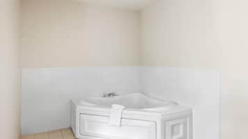 A corner bathroom with a white bathtub, tiled walls, and floor.