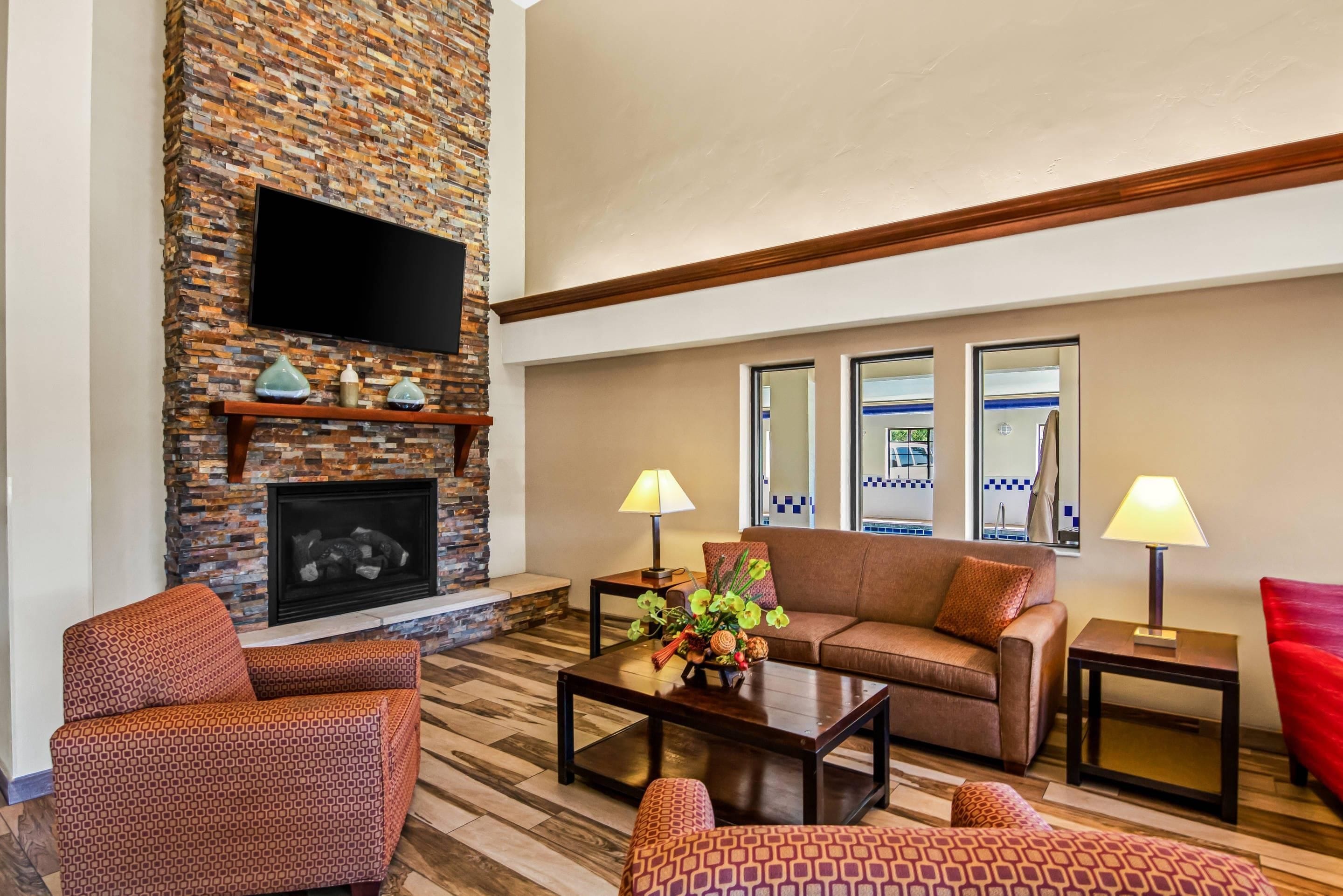 A living room with a brick fireplace, a flat-screen TV, a sofa, two armchairs, a coffee table, and two lamps.