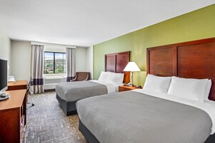 Camera d'albergo con due letti, una scrivania con un computer, una lampada e vista sull'esterno.