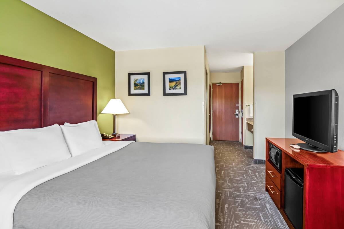 A hotel room with a bed, a TV, a lamp, and two framed pictures on the wall.