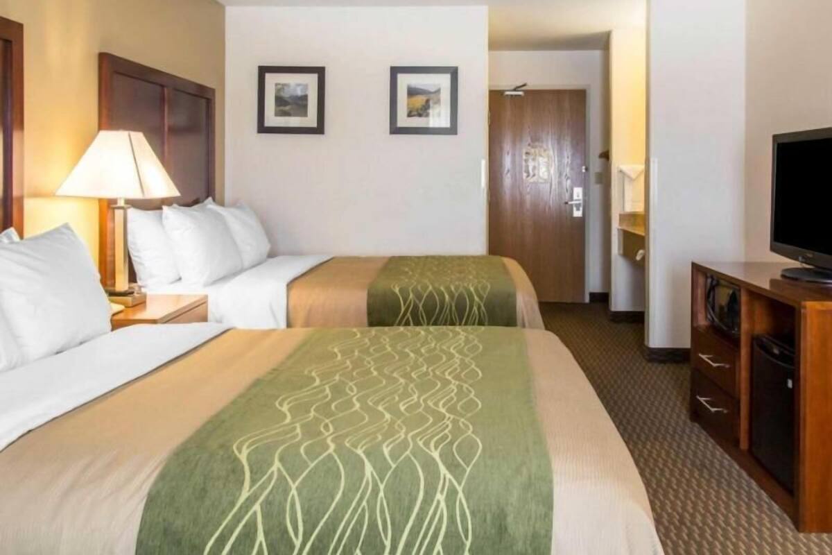 A hotel room with two beds, a TV, a desk, and a door leading to another room.