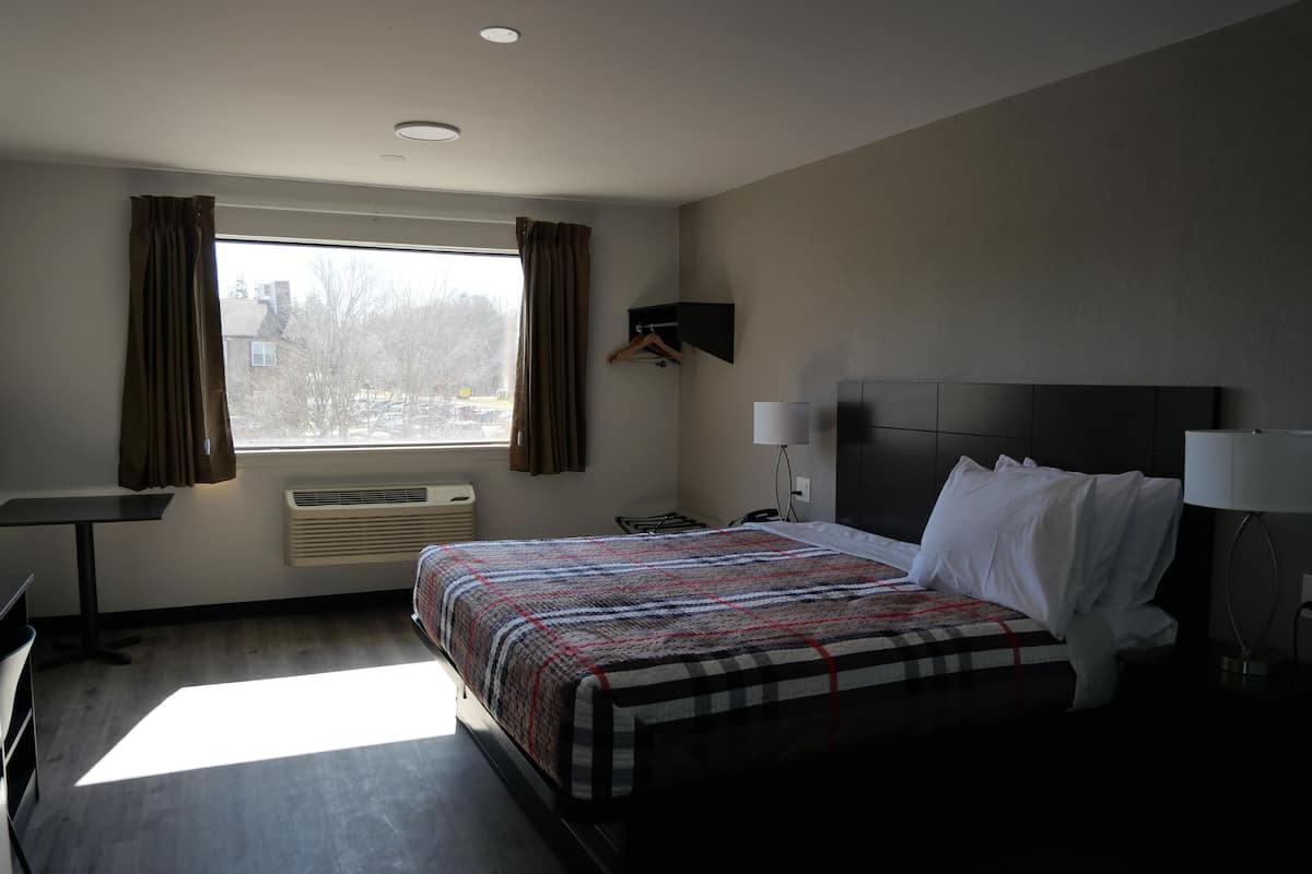 A hotel room with a bed, bedside lamps, a desk, and a window with curtains.