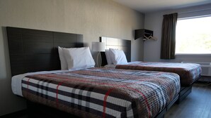 A hotel room with a large bed, two bedside tables, a wall-mounted lamp, and a window with curtains.