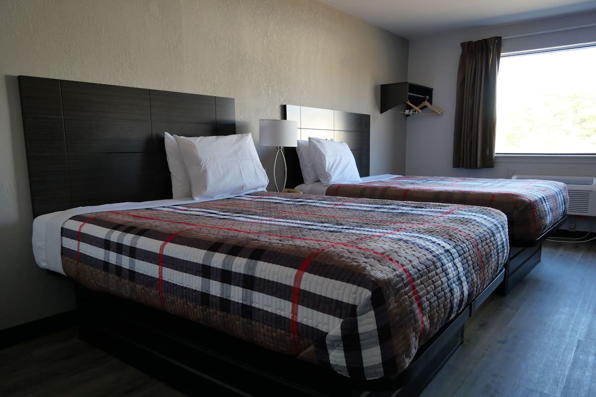 A hotel room with a large bed, two bedside tables, a wall-mounted lamp, and a window with curtains.