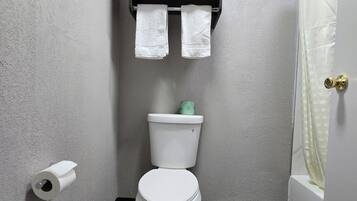 Une salle de bain comprenant des toilettes, un porte-serviettes avec trois serviettes, un rouleau de papier toilette et un rideau de douche.