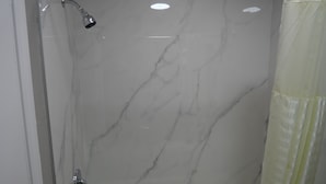 A bathroom with a bathtub, a shower, and a marble wall.