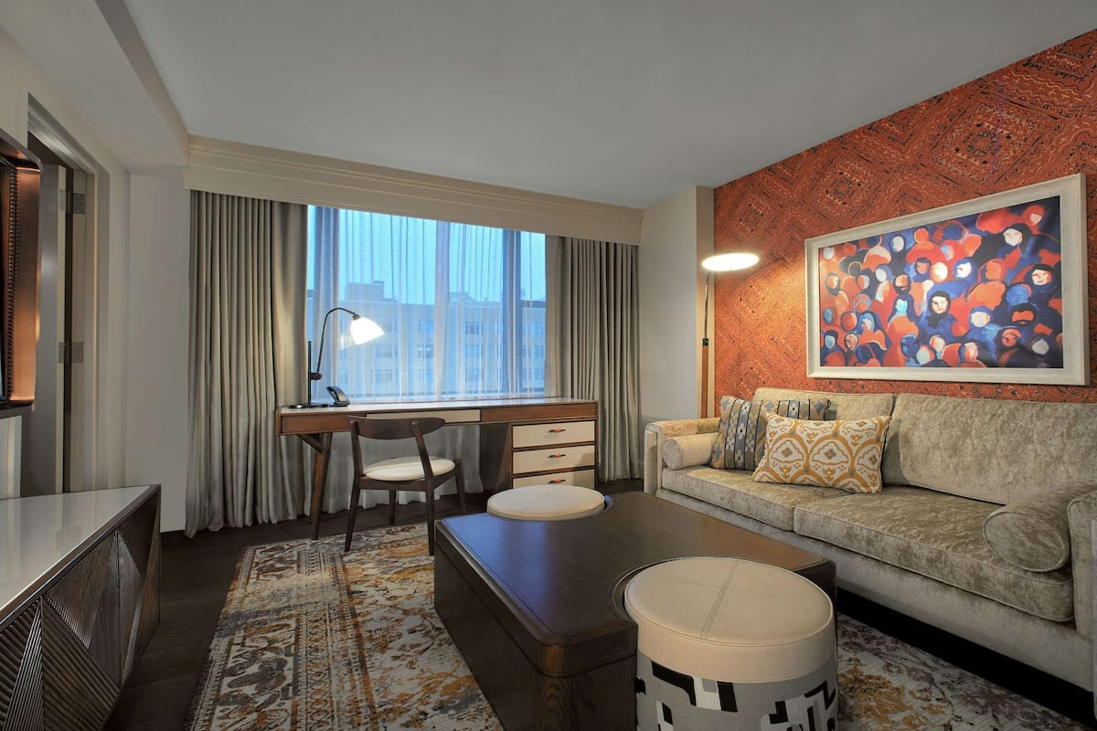 A modern living room with a sofa, a desk, a chair, a lamp, and a large abstract painting on the wall.