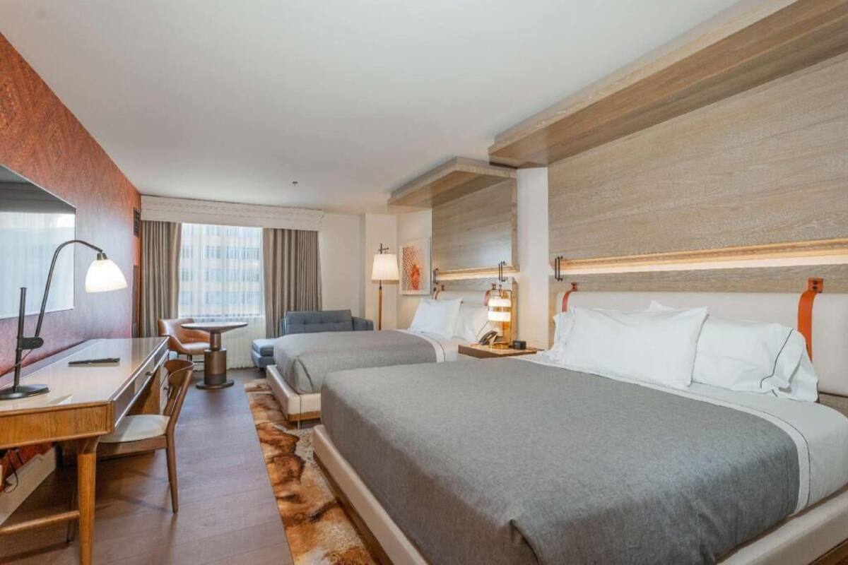 A hotel room with two beds, a desk, a chair, a lamp, and a window with curtains.