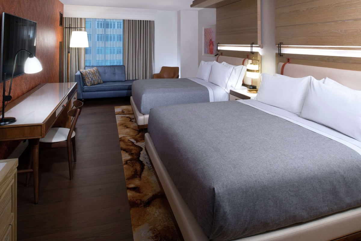 A hotel room with two beds, a desk, a chair, a TV, and a window with curtains.