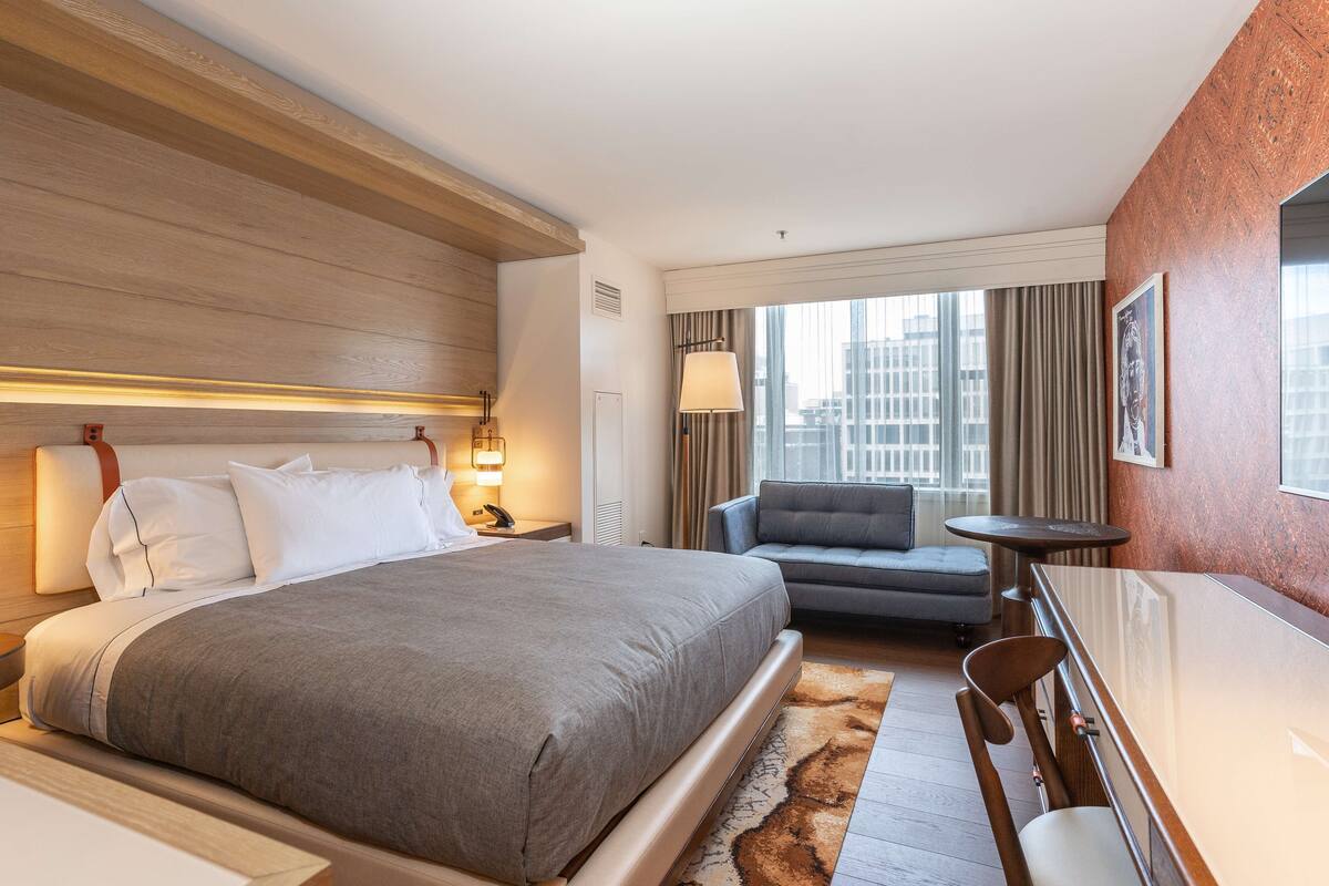 A hotel room with a large bed, a sofa, a small table, and a view of the city.
