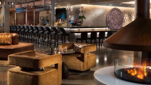 A modern bar area with a brick wall, bar stools, and a large fire feature. - Canopy by Hilton Washington Embassy Row (Washington)