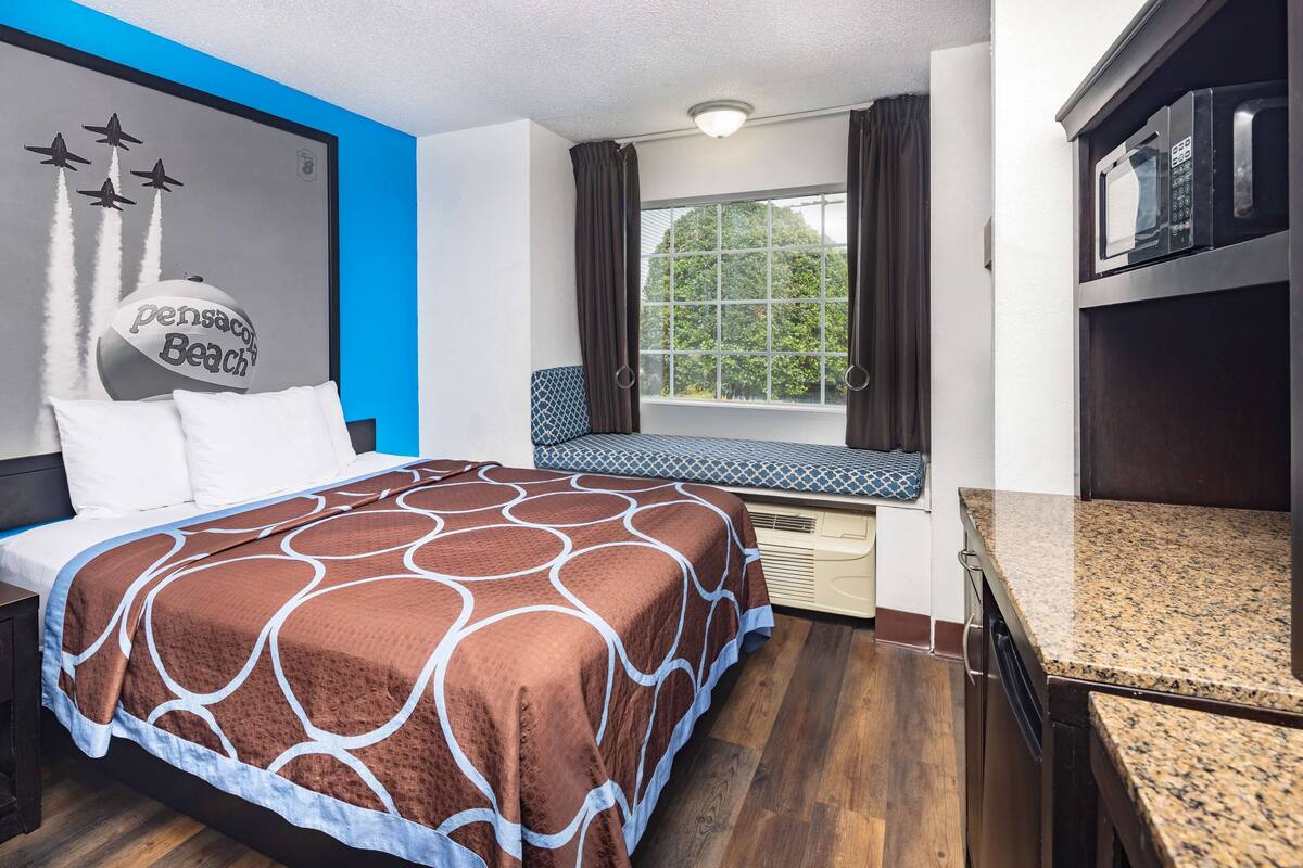 Habitación de hotel con cama, un banco junto a la ventana, microondas y un mural con un dibujo de un jet.