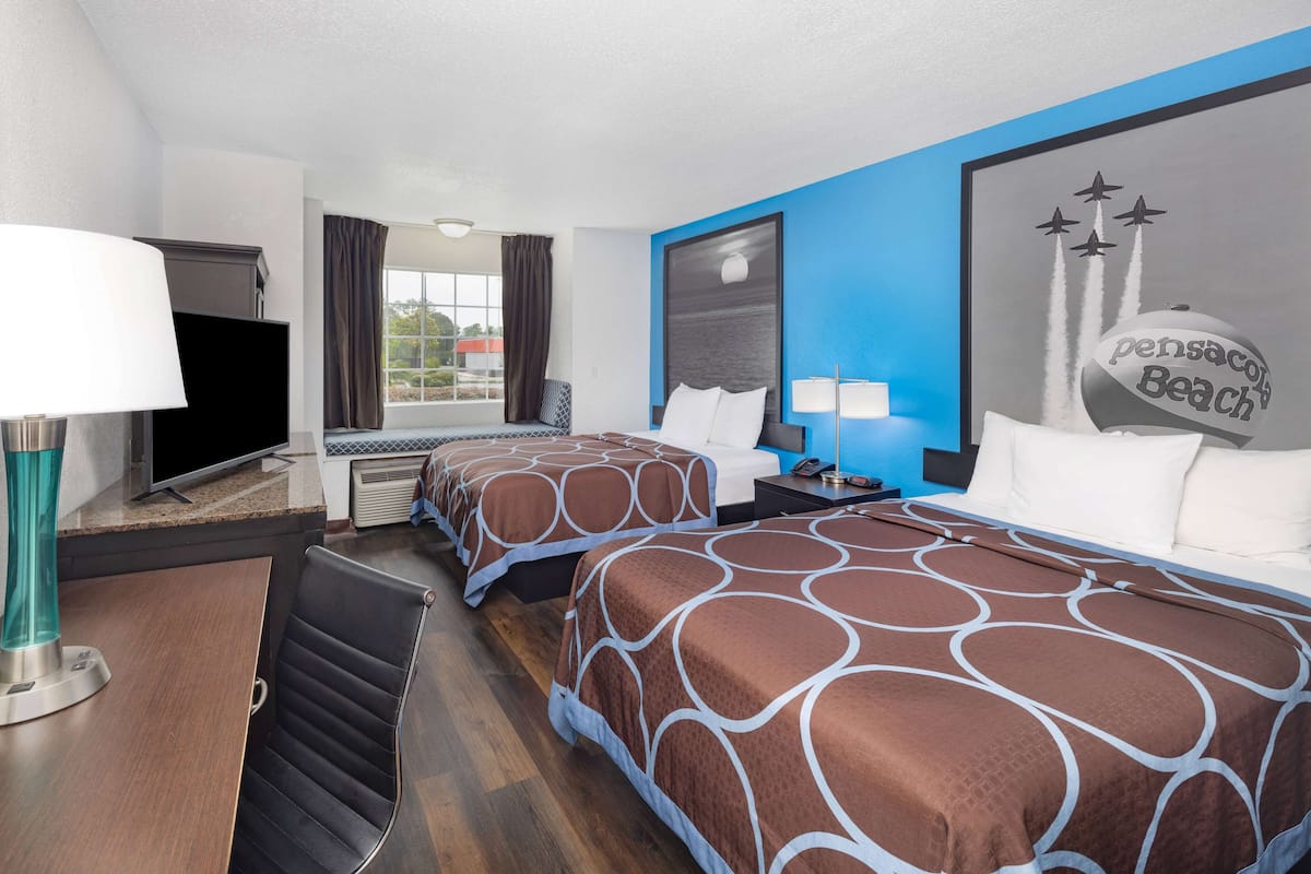 Habitación de hotel con dos camas, televisión, escritorio y ventana con cortinas.