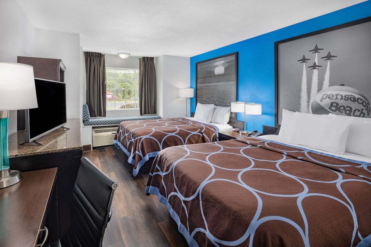 Habitación de hotel con dos camas, un escritorio, un televisor y un amplio ventanal con cortinas.