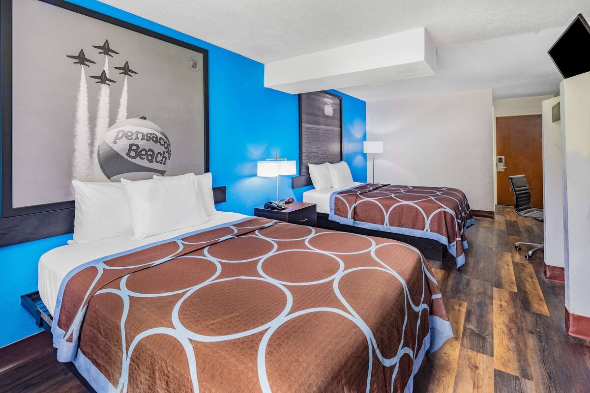 Habitación de hotel con dos camas, una obra de arte grande de aviones en un balón de playa, y una pared azul decorativa.