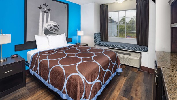 Ein Hotelzimmer mit einem großen Bett, einer Sitzgelegenheit am Fenster, einem Wandbild und Blick ins Freie.