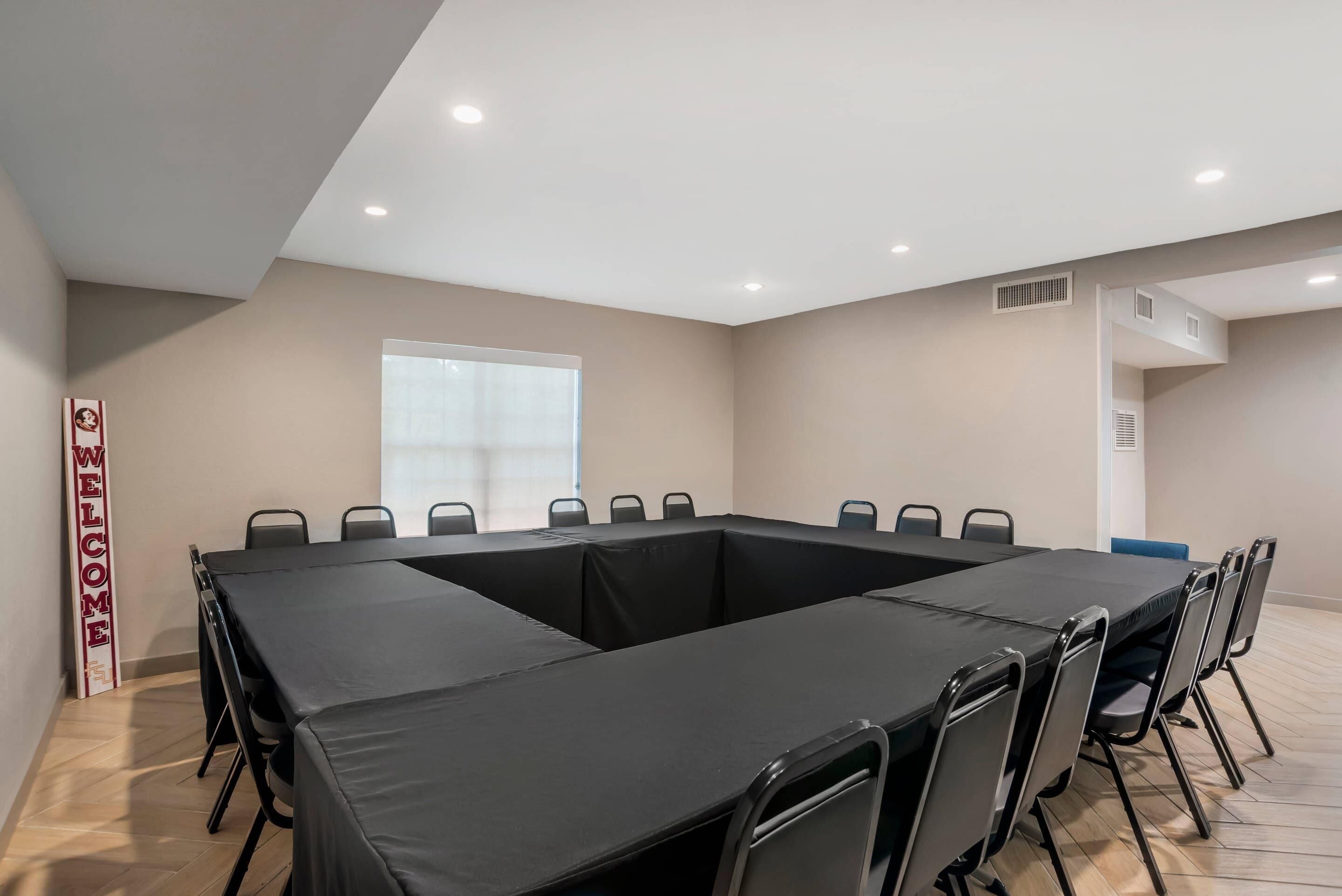 Un salón de conferencias con una gran mesa, sillas, un cartel que dice 'WELCOME', una ventana y luces empotradas en el techo.