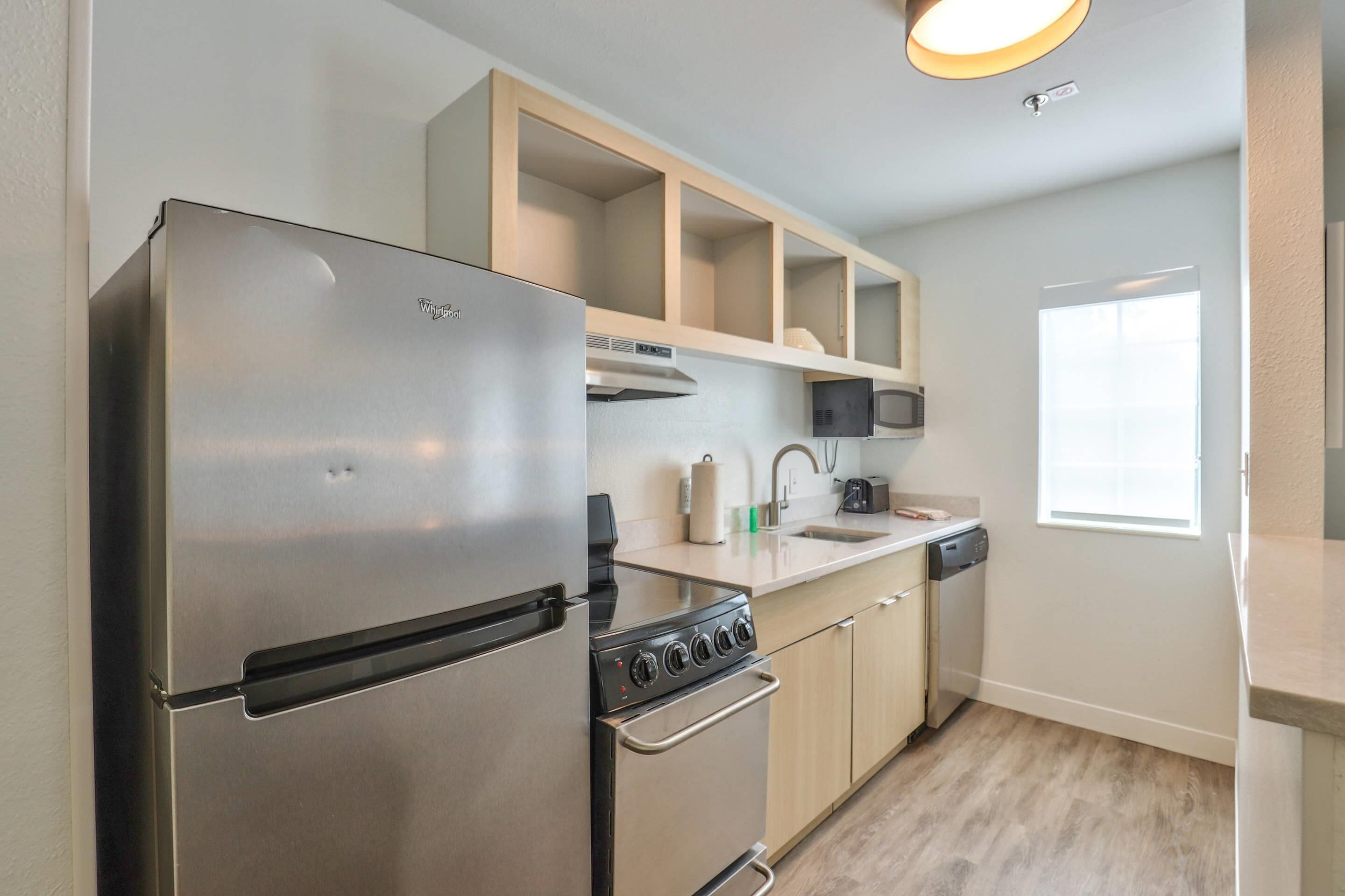 A modern kitchen with a stainless steel refrigerator, a built-in oven, wooden cabinets, a microwave, and a dishwasher.