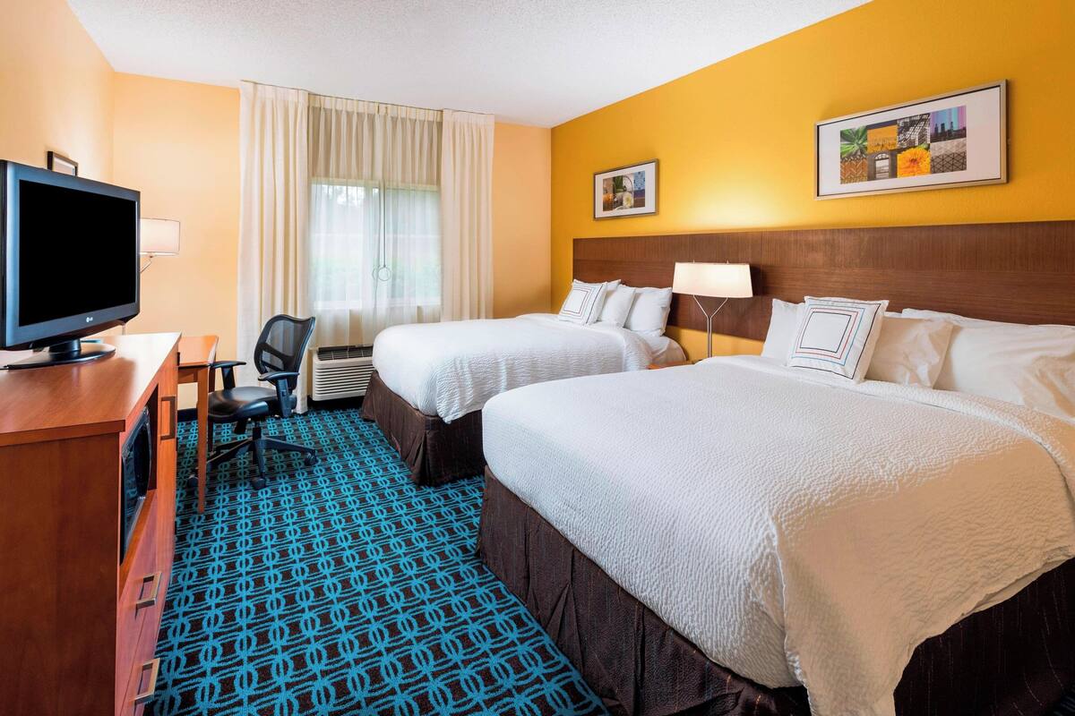 A hotel room with two beds, a desk with a computer, a chair, and a television.