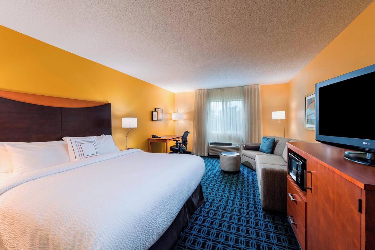 A hotel room with a large bed, a desk, a television, and a sofa.