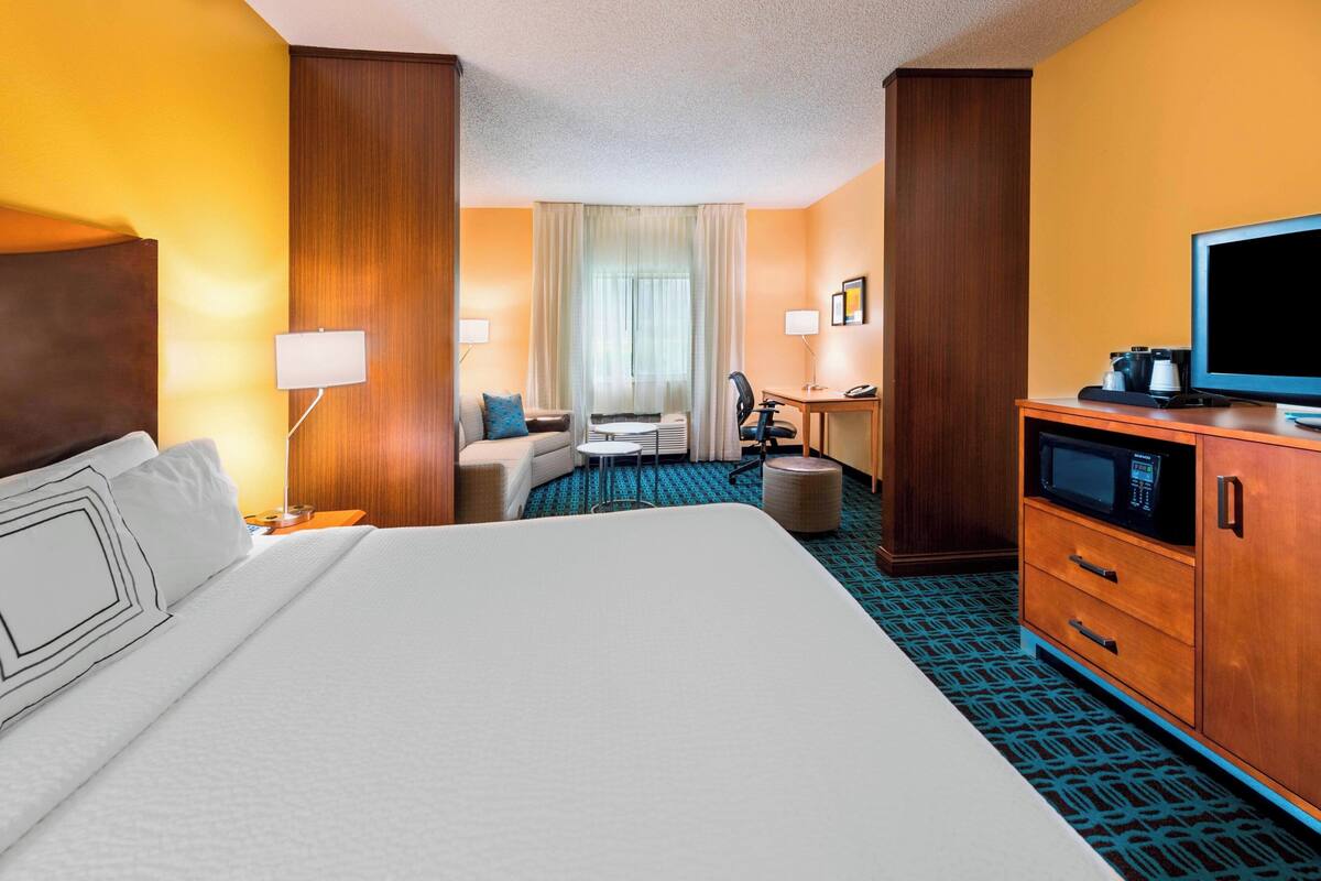 A hotel room with a large bed, a desk, a chair, a television, and a microwave.