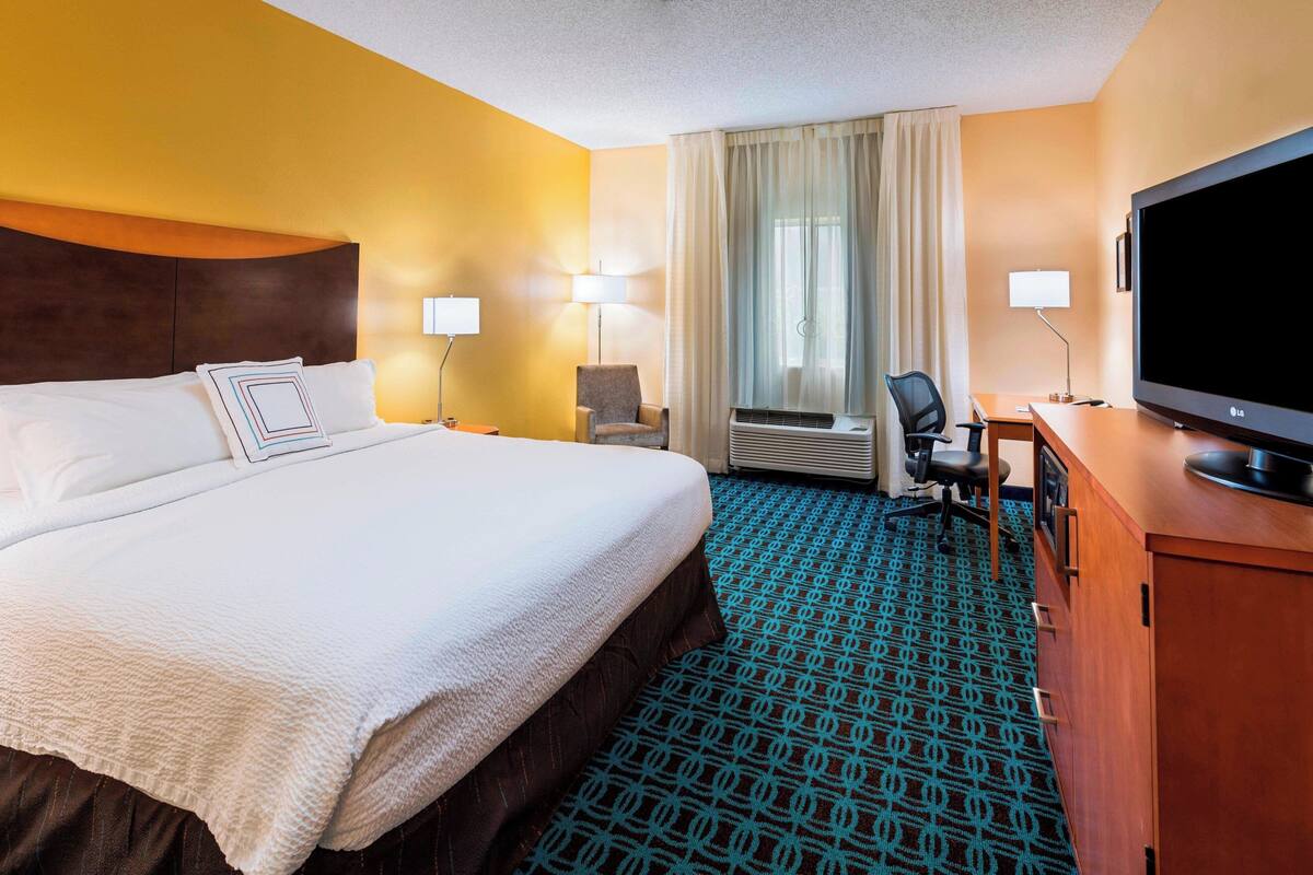 A hotel room with a large bed, a desk with a television, and a chair.