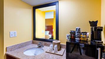 A hotel bathroom with a sink, mirror, coffee machine, and toiletries.