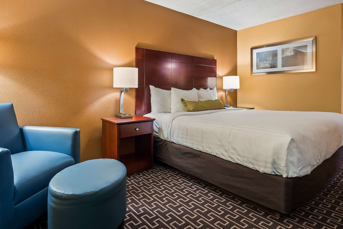 Una habitación de hotel con una cama, una silla, una mesita de noche y una lámpara.