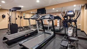 Een sportschool met loopbanden, elliptische trainers en een gewichtsapparaat.