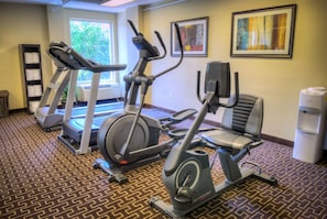 A gym with treadmills, an elliptical, and a stationary bike. There is a water cooler and a wall-mounted shelf with towels.