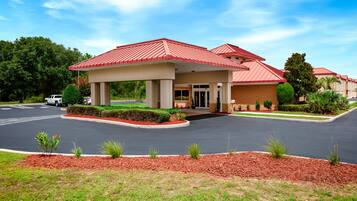 A hotel with a red roof, a covered entrance, and a landscaped driveway.