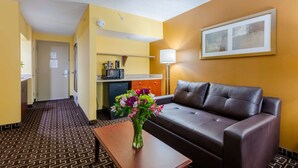 Een hotelkamer met een bruine leren bank, een klein houten tafeltje met een bloevas, een magnetron en een lamp.