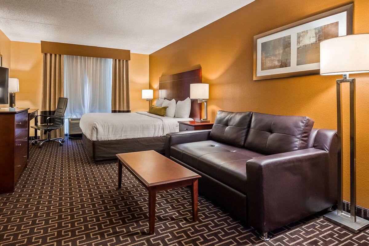 Una habitación de hotel con cama, sofá, escritorio, televisor y lámpara.