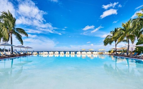 A large, clear swimming pool with lounge chairs and umbrellas, surrounded by palm trees.