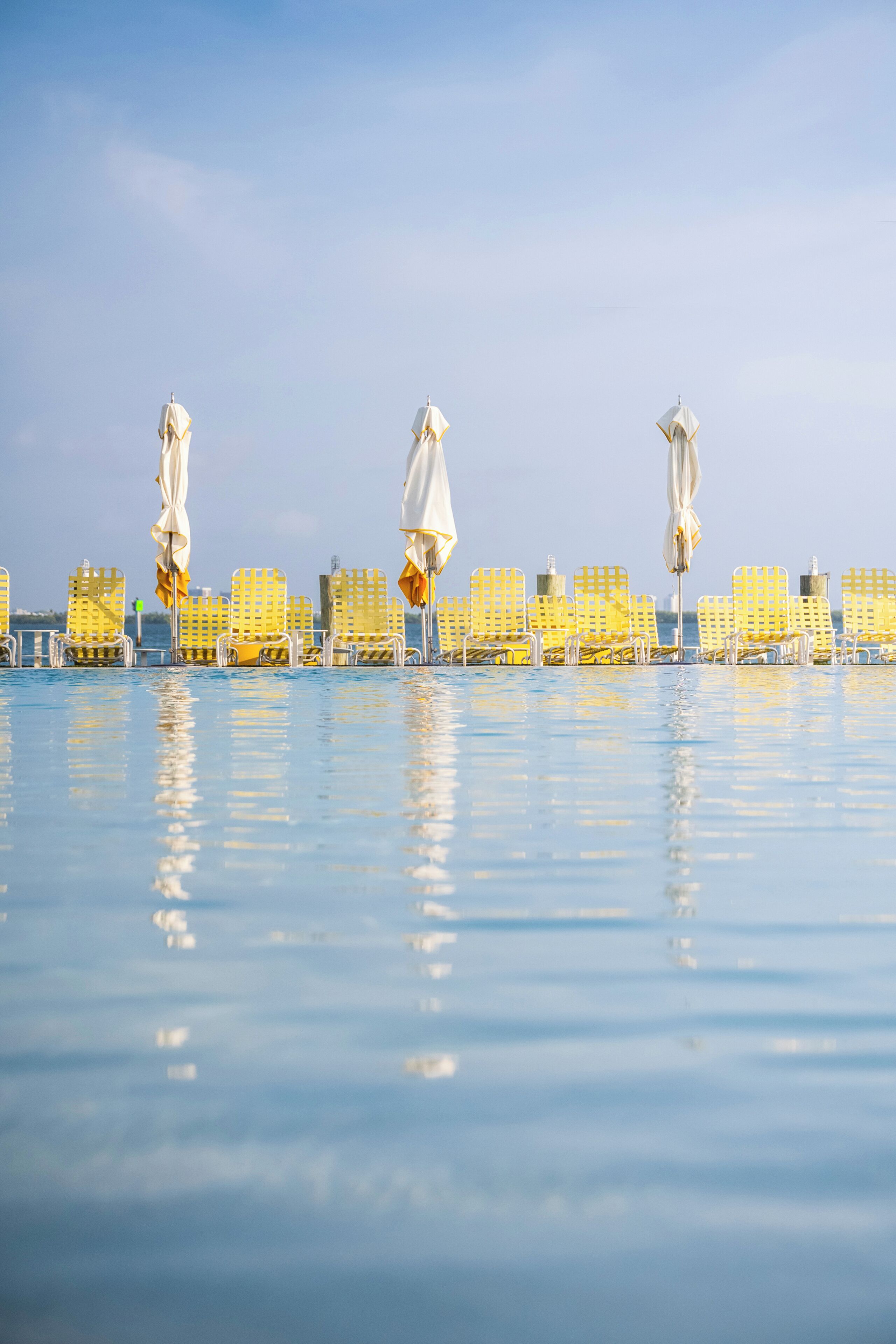 A poolside area with yellow lounge chairs and white umbrellas.