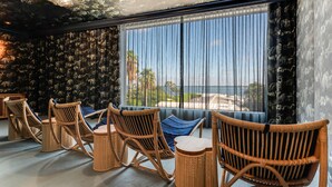 Una habitación con mobiliario de mimbre, un ventanal con cortinas y vistas a palmeras.