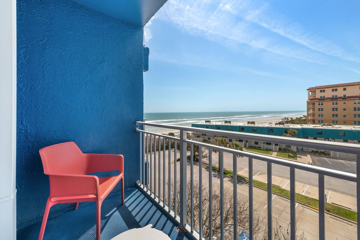 Un balcon avec une chaise rouge, une vue sur la plage et un parking.