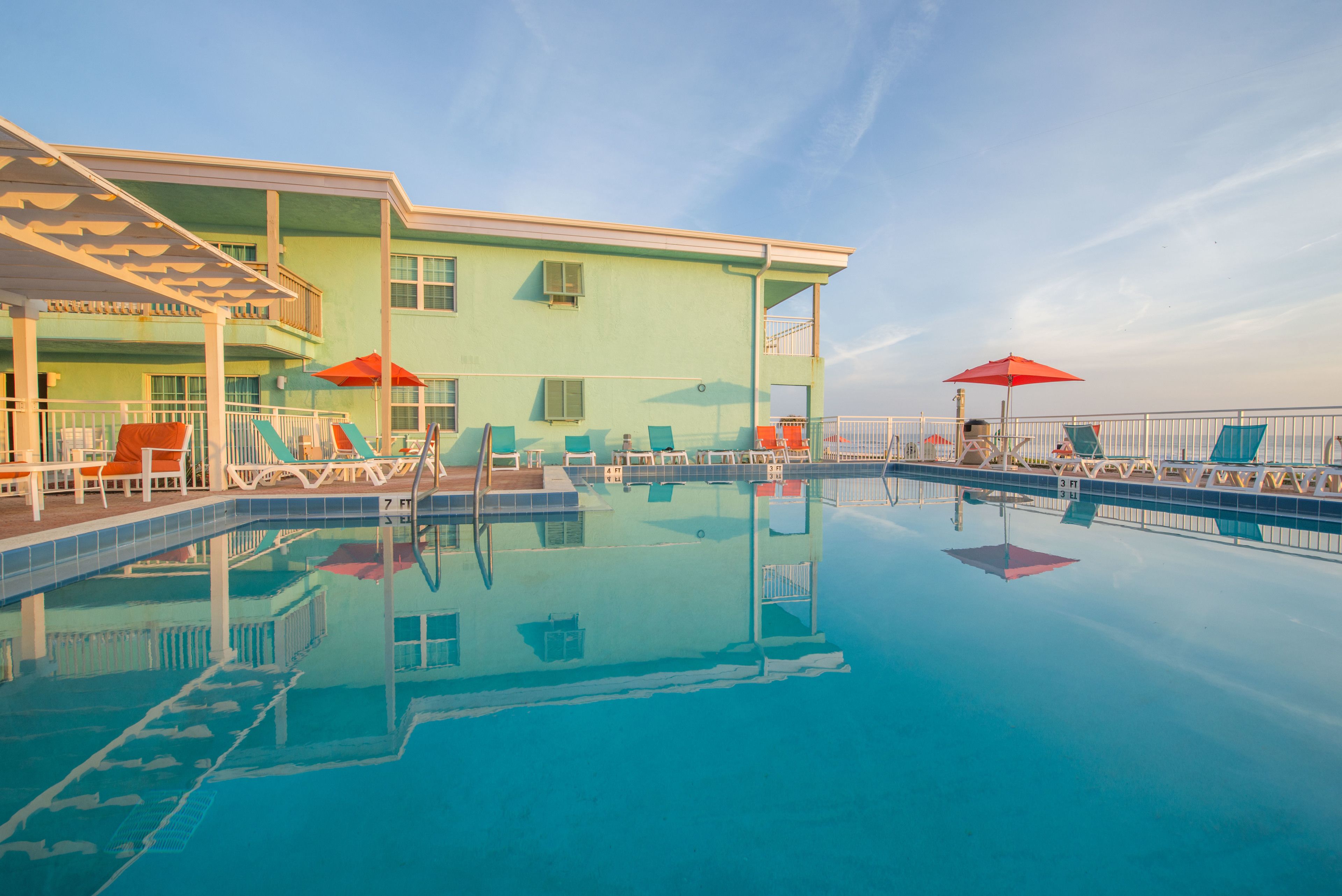 A swimming pool with lounge chairs and umbrellas, a building with a balcony, and a clear sky.