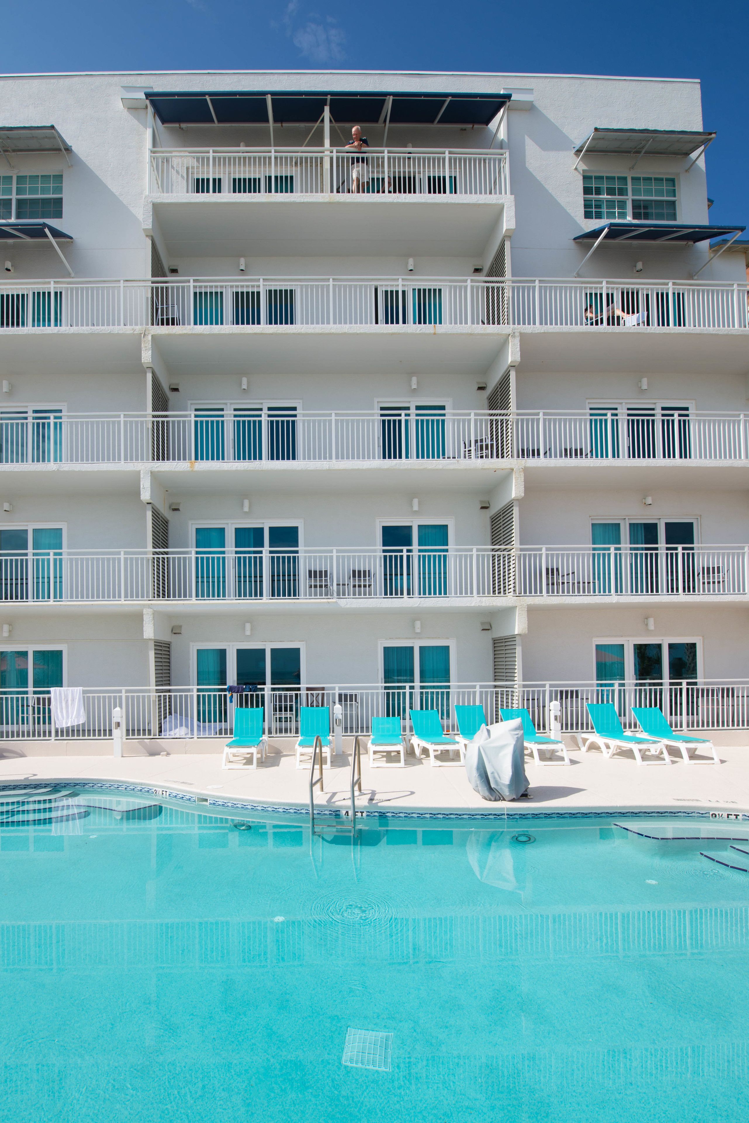 Un hotel de varios pisos con balcones, piscina y tumbonas.