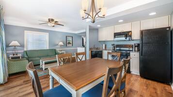 Une cuisine moderne avec un réfrigérateur noir, des armoires blanches et un coin repas comprenant une table en bois et des chaises bleues.
