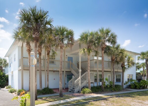 A two-story building with a central staircase, surrounded by palm trees.