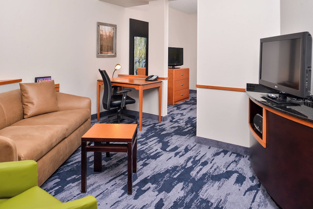 A hotel room with a sofa, a desk with a chair, a television, and a small table.