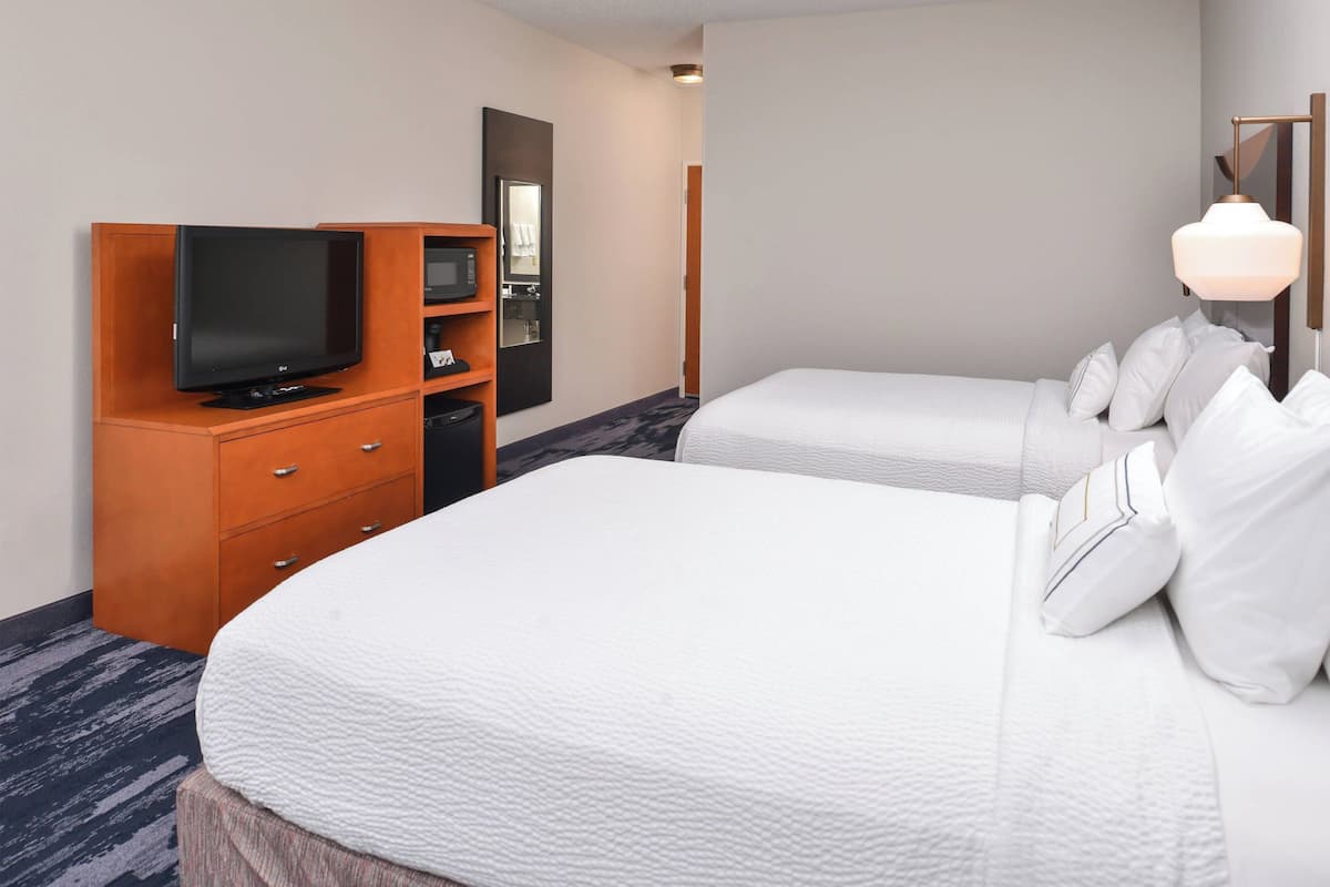 A hotel room with two beds, a television, a minibar, and a mirror.