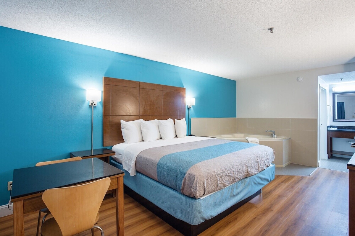 A hotel room with a bed, bedside table, chair, and a bathroom with a bathtub and sink.