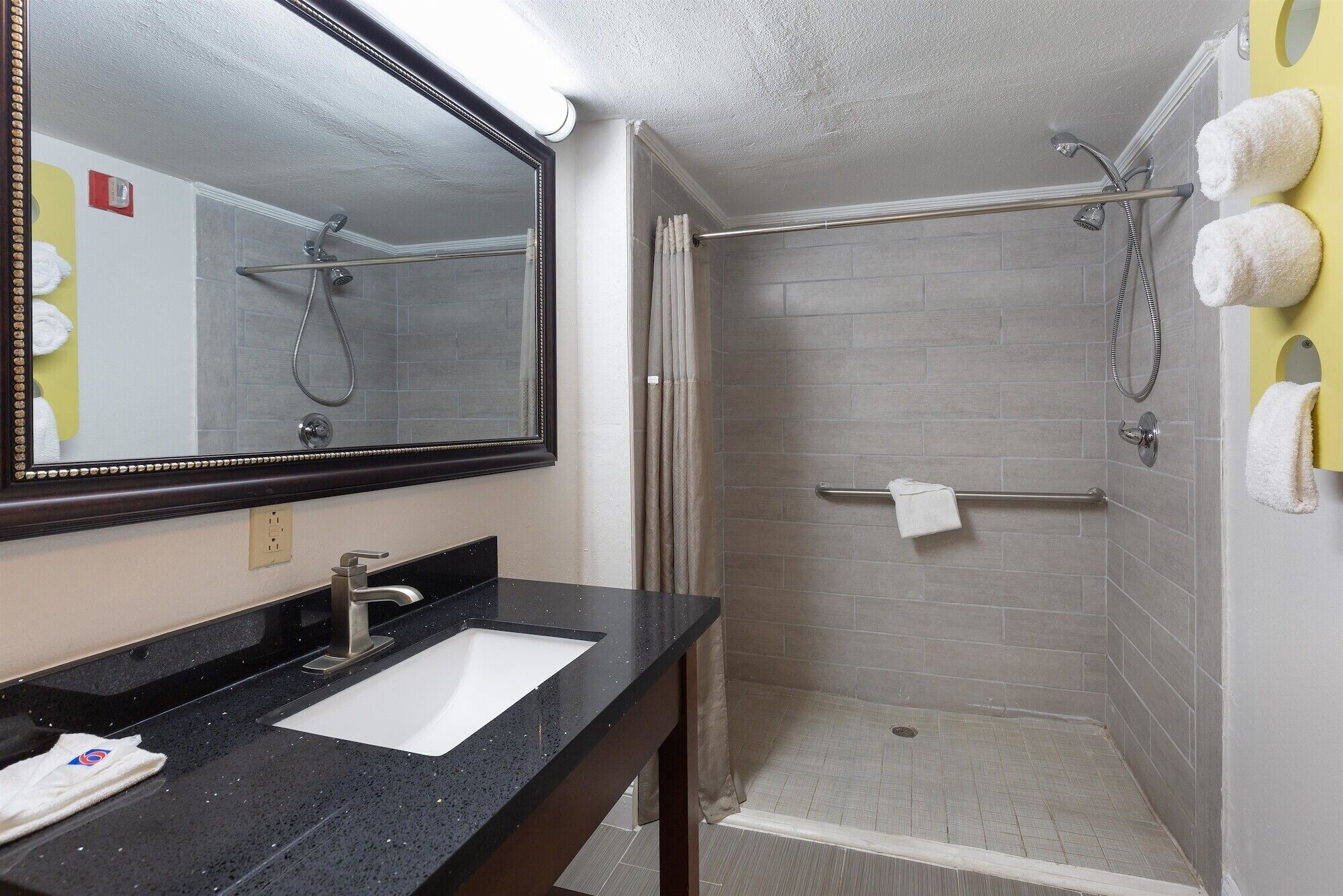 Un bagno moderno con lavabo su piano nero, uno specchio grande e zona doccia con porta in vetro.