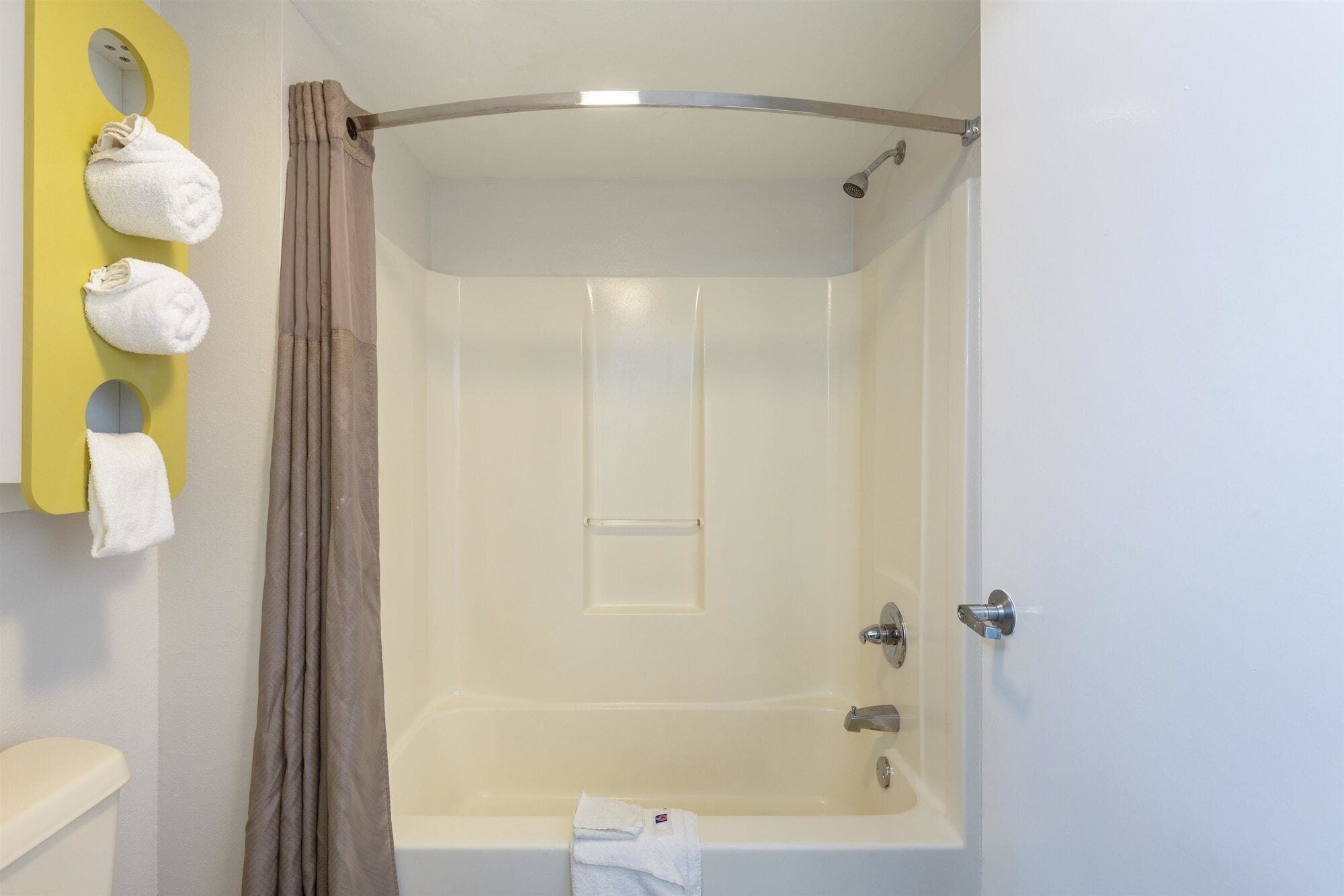 Ein Badezimmer mit einer Badewanne, einer Duschvorhang und Handtüchern, die an einer gelben Wand hängen.